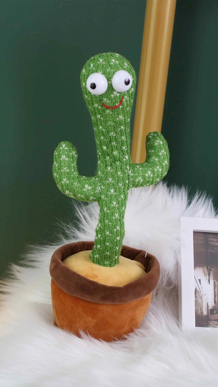 green background, white feather blanket, photograph frame, yellow bamboo stick lamp, brown flowerpot, green singing dancing cactus, dancing cactus toy, voice activated cactus, talkback speaking cactus, talking baby cactus toy, white big eyes,